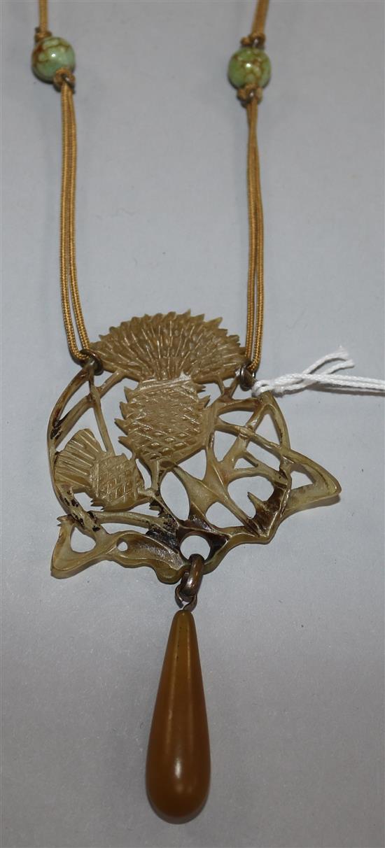 A horn drop pendant carved with a thistle and signed Cis?, on a fabric necklace with six beads.